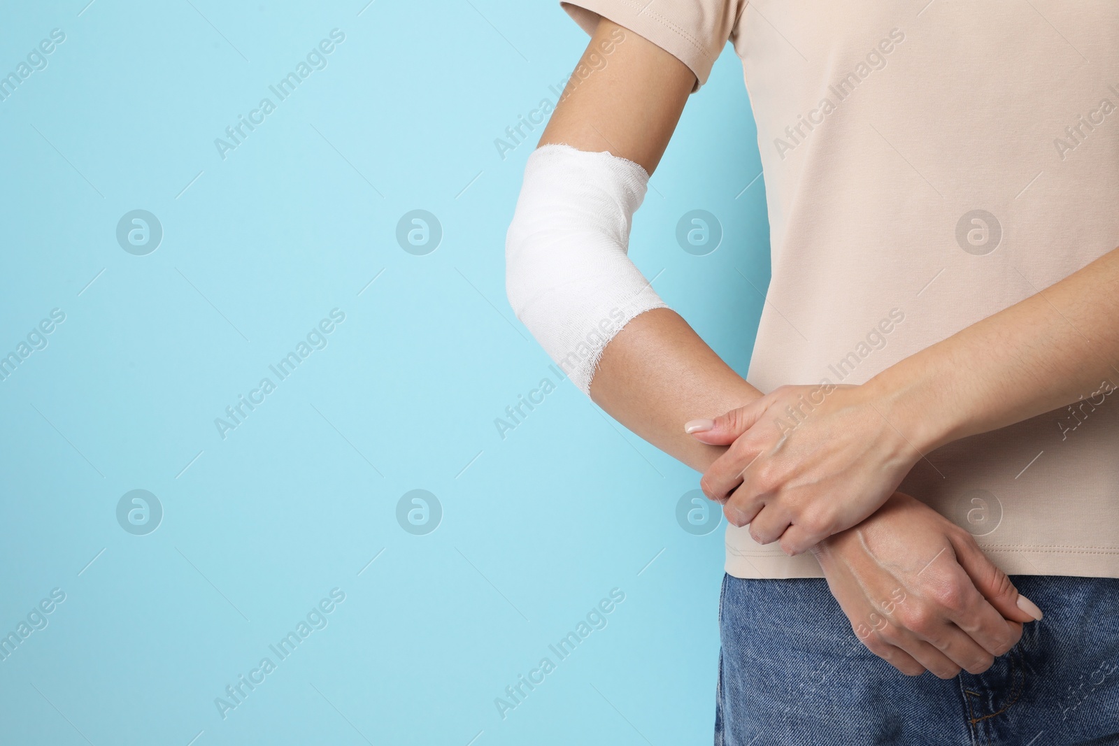 Photo of Woman with medical bandage on elbow against light blue background, closeup. Space for text