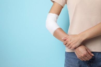 Photo of Woman with medical bandage on elbow against light blue background, closeup. Space for text