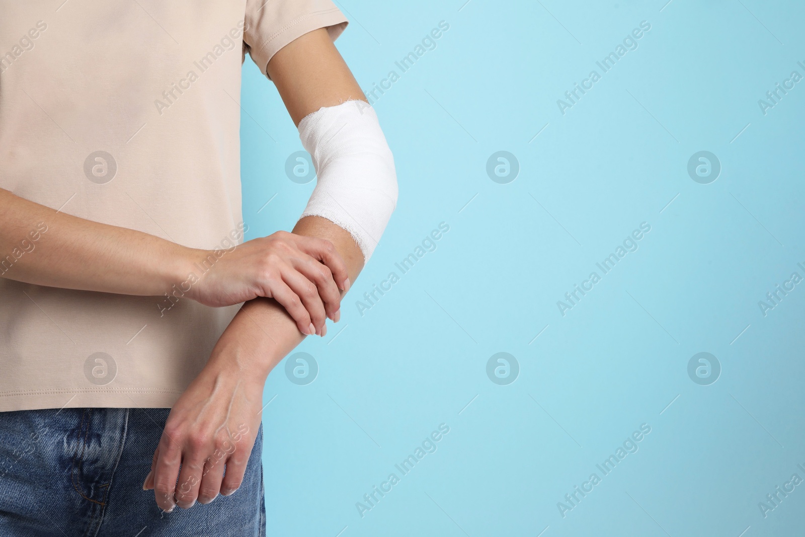 Photo of Woman with medical bandage on elbow against light blue background, closeup. Space for text