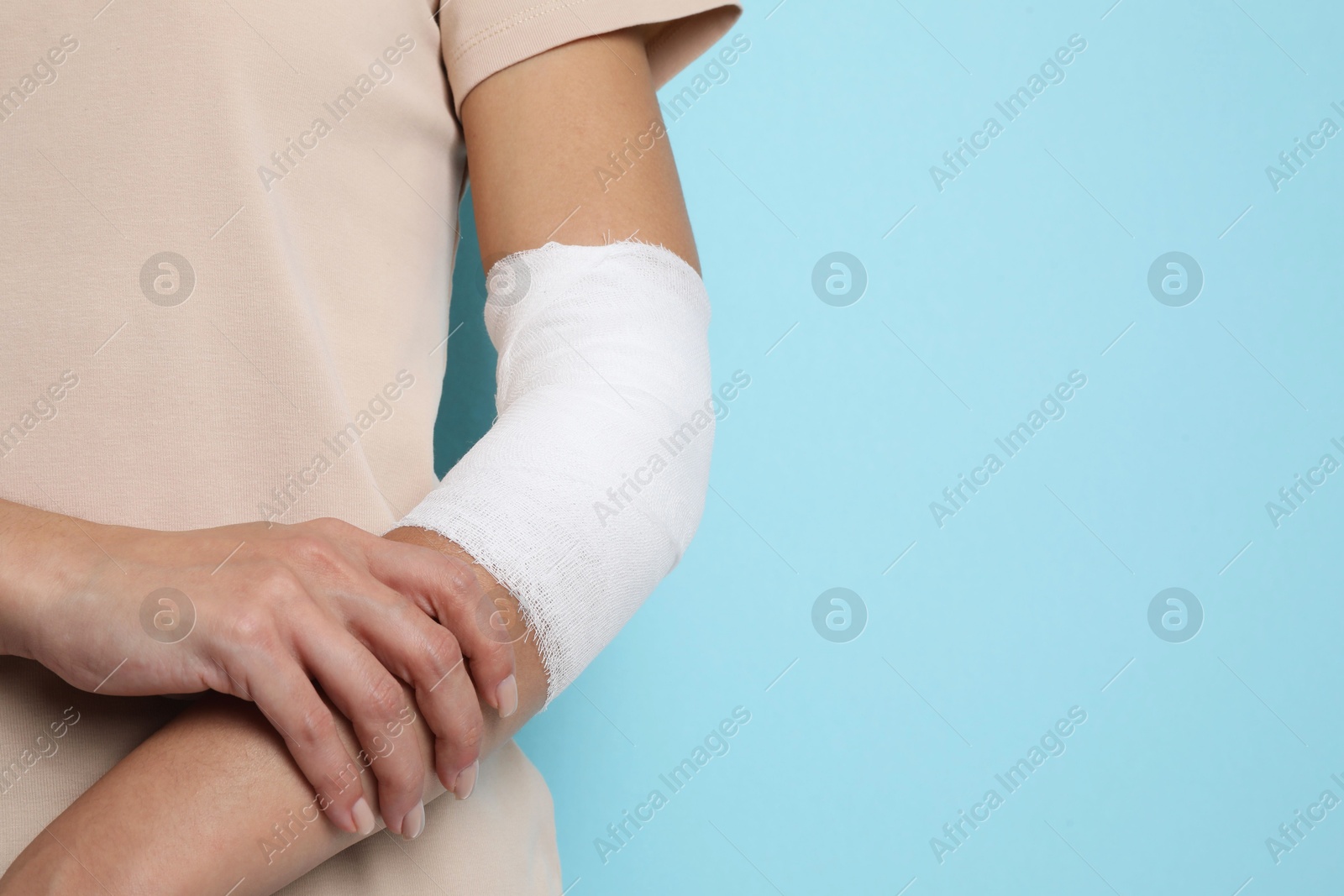 Photo of Woman with medical bandage on elbow against light blue background, closeup. Space for text