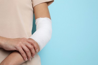 Photo of Woman with medical bandage on elbow against light blue background, closeup. Space for text