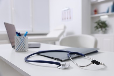 Photo of Laptop, stethoscope and folders on desk in medical office, closeup