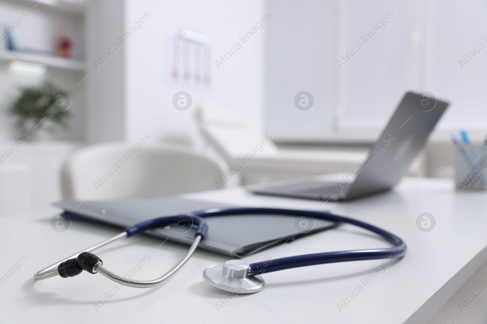 Photo of Laptop, stethoscope and folders on desk in medical office, closeup