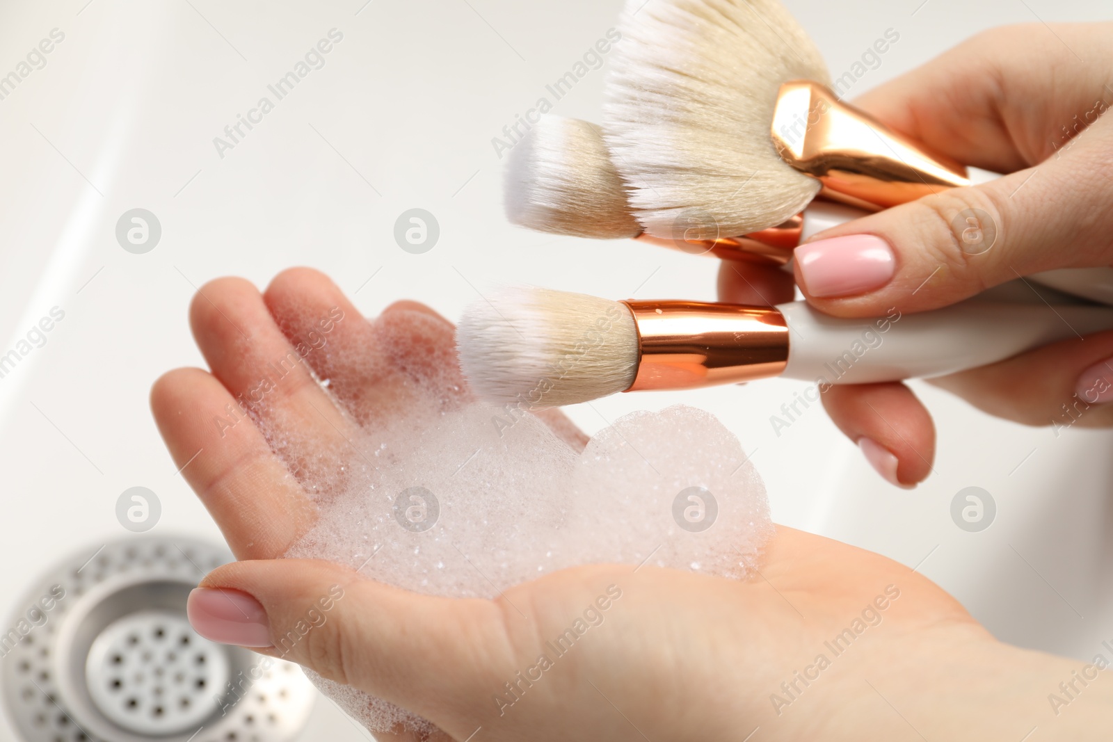 Photo of Woman washing makeup brushes with soap over sink, closeup