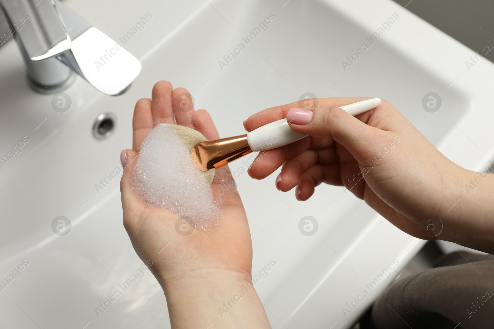 Photo of Woman washing makeup brush with soap over sink, above view