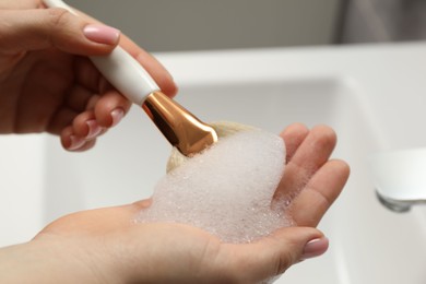 Photo of Woman washing makeup brush with soap over sink, closeup