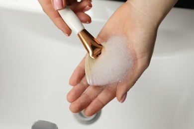 Photo of Woman washing makeup brush with soap over sink, above view