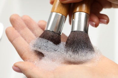 Photo of Woman washing makeup brushes with soap, closeup