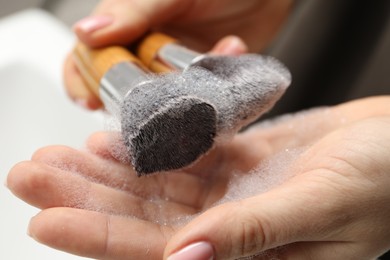 Photo of Woman washing makeup brushes with soap, closeup