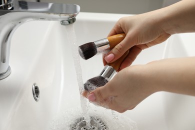 Photo of Woman washing makeup brushes under stream of water in sink, closeup