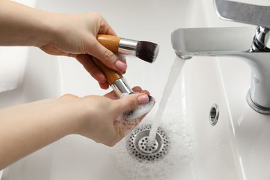 Photo of Woman washing makeup brushes under stream of water in sink, closeup