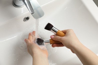 Photo of Woman washing makeup brushes under stream of water in sink, above view