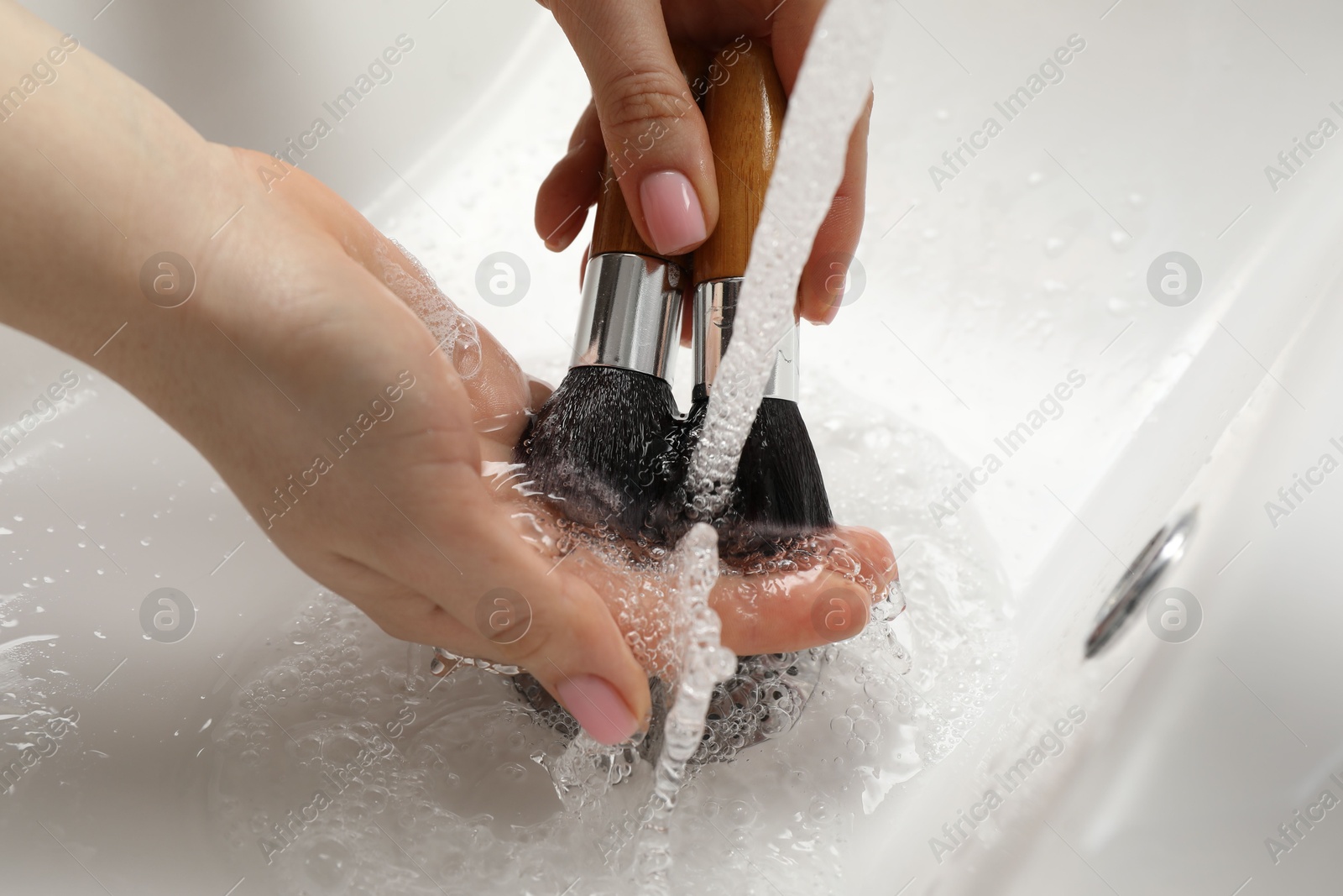 Photo of Woman washing makeup brushes under stream of water in sink, closeup