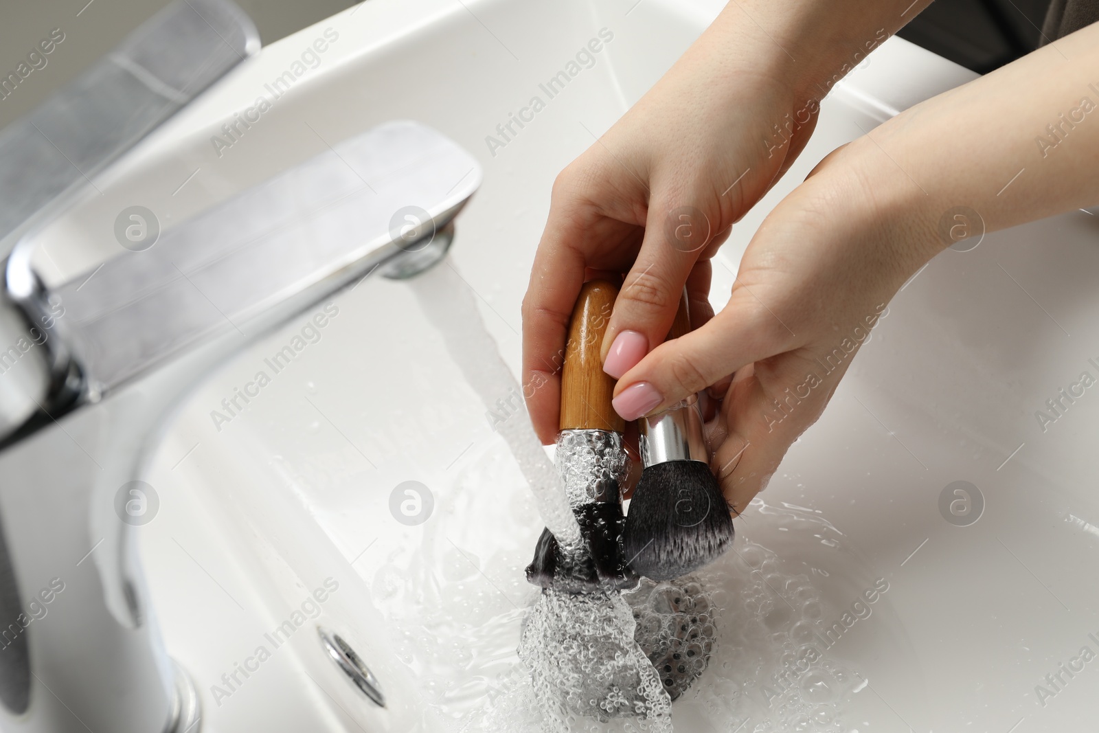 Photo of Woman washing makeup brushes under stream of water in sink, closeup