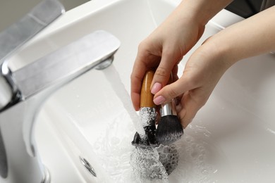 Photo of Woman washing makeup brushes under stream of water in sink, closeup