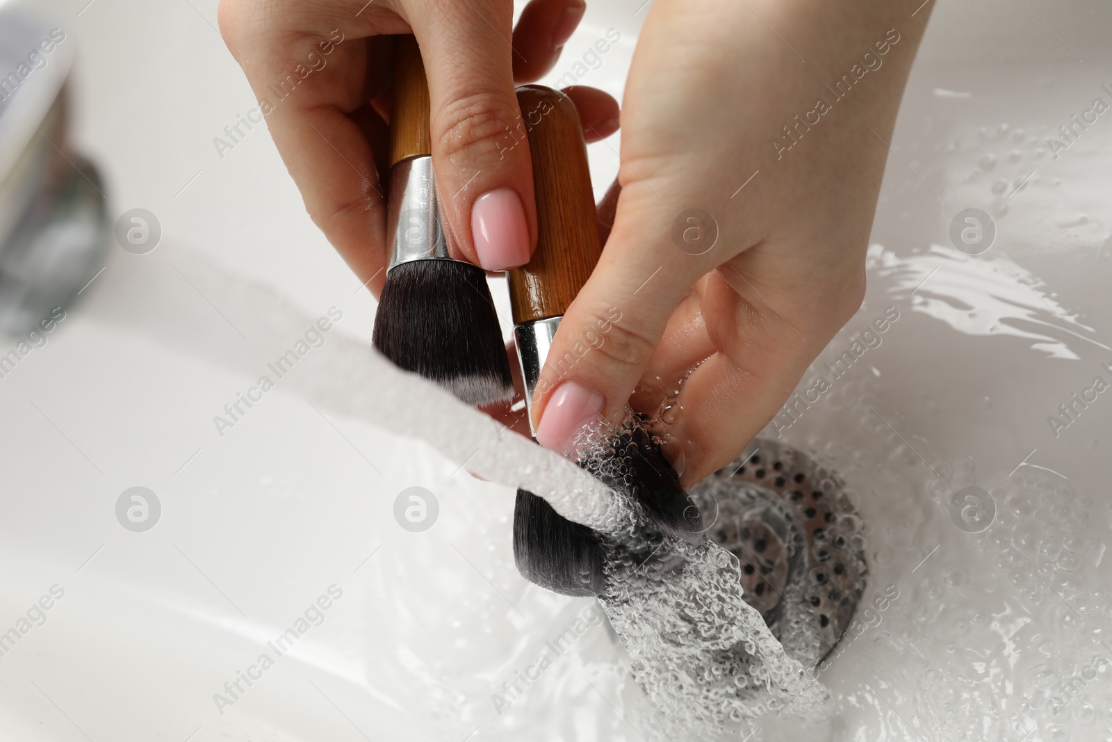 Photo of Woman washing makeup brush under stream of water in sink, above view