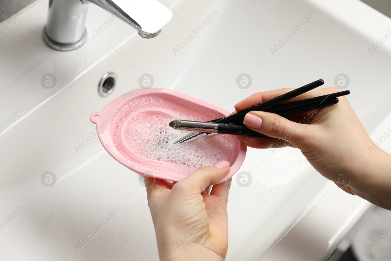 Woman washing makeup brushes with soap and cleansing pad over sink, above view Photo of Woman washing makeup brushes with soap and cleansing pad over sink, above view