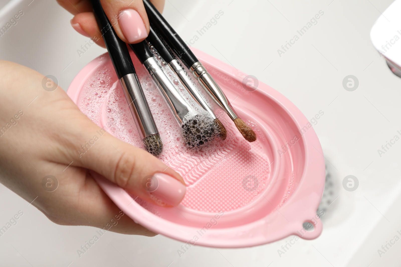 Photo of Woman washing makeup brushes with soap and cleansing pad in sink, closeup