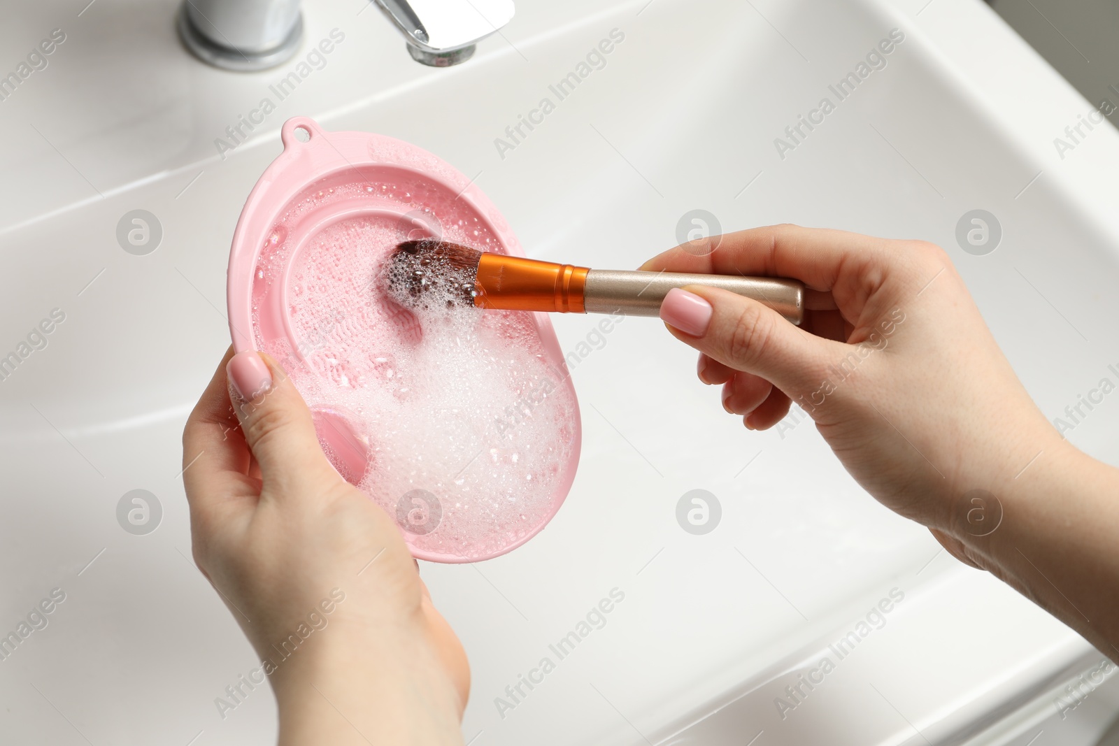 Photo of Woman washing makeup brush with soap and cleansing pad over sink, above view