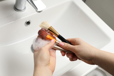 Photo of Woman washing makeup brushes with soap over sink, above view