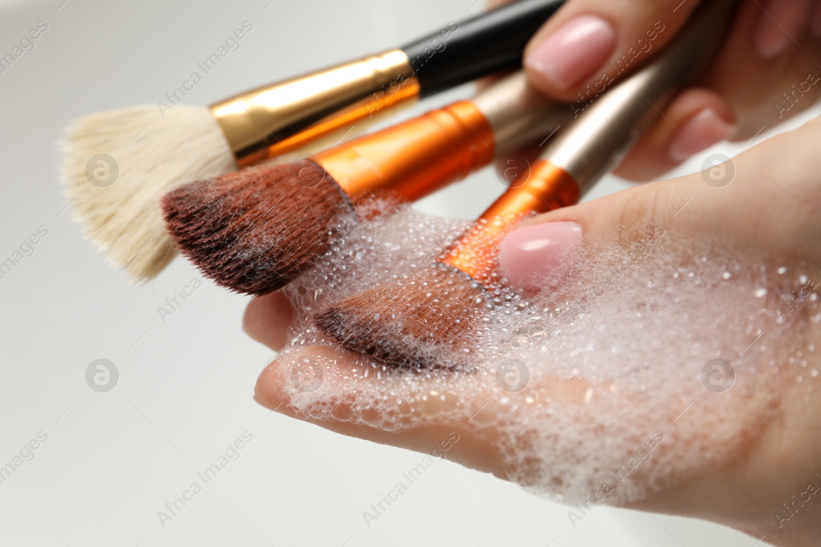 Photo of Woman washing makeup brush with soap on light background, closeup