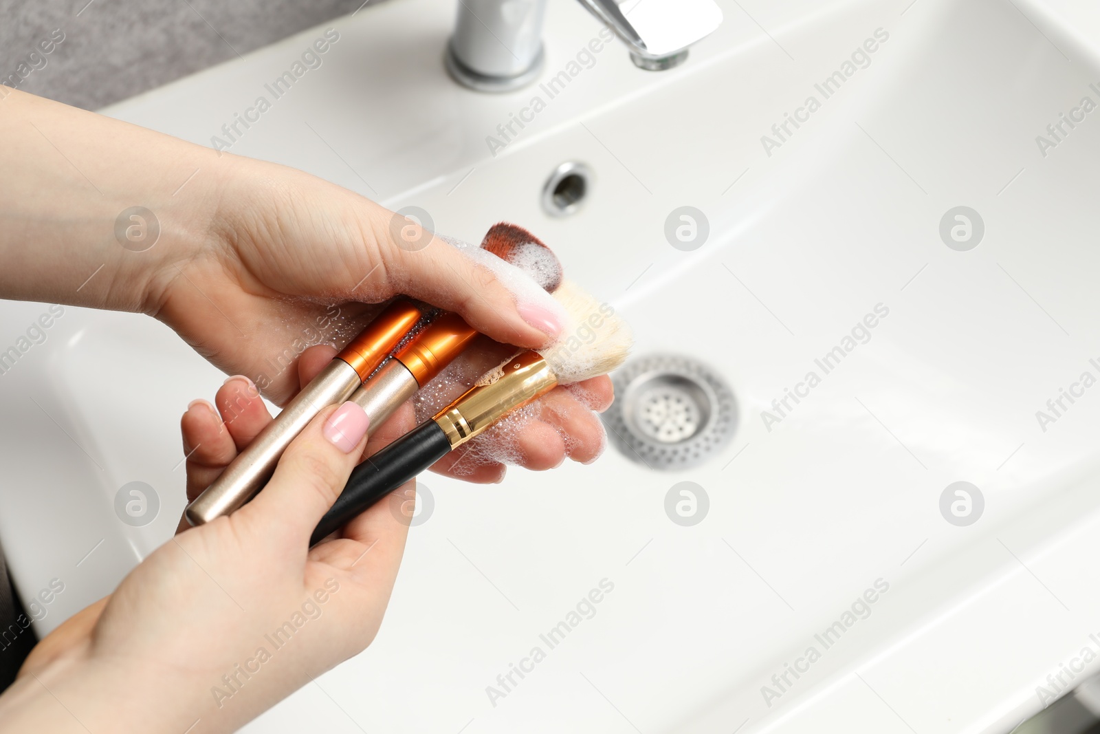 Photo of Woman washing makeup brush with soap over sink, above view. Space for text