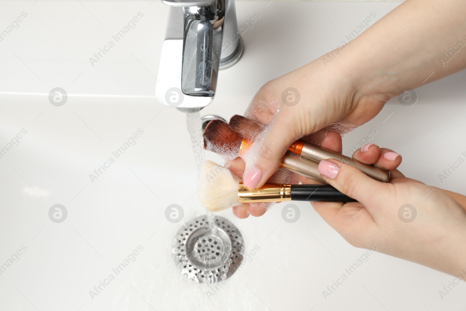 Photo of Woman washing makeup brush under stream of water in sink, above view