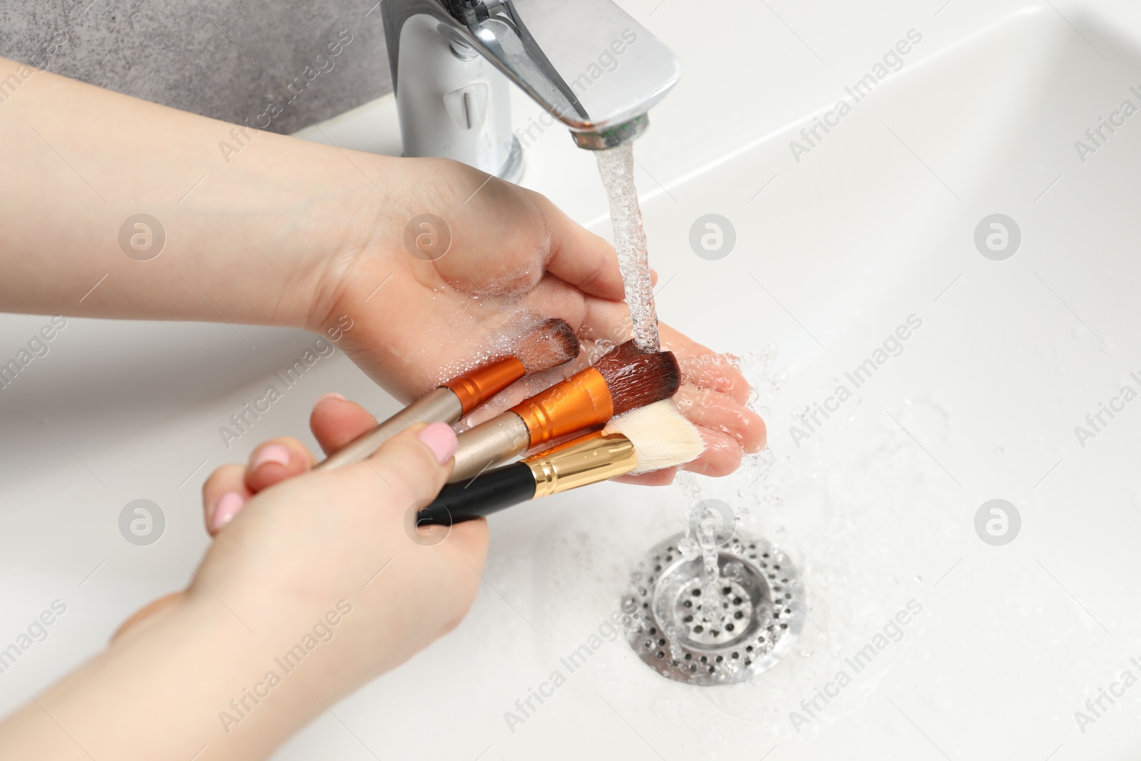 Photo of Woman washing makeup brush under stream of water in sink, closeup