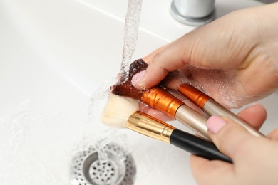 Photo of Woman washing makeup brush under stream of water in sink, closeup