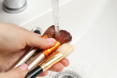 Photo of Woman washing makeup brush under stream of water in sink, closeup