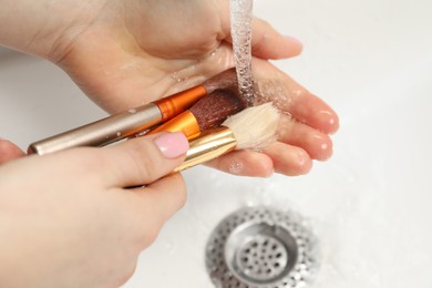 Photo of Woman washing makeup brush under stream of water in sink, closeup