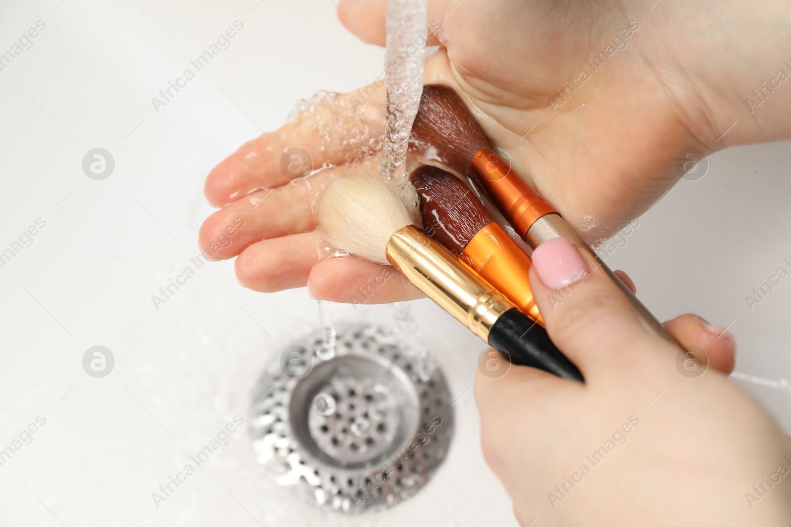 Photo of Woman washing makeup brush under stream of water in sink, closeup