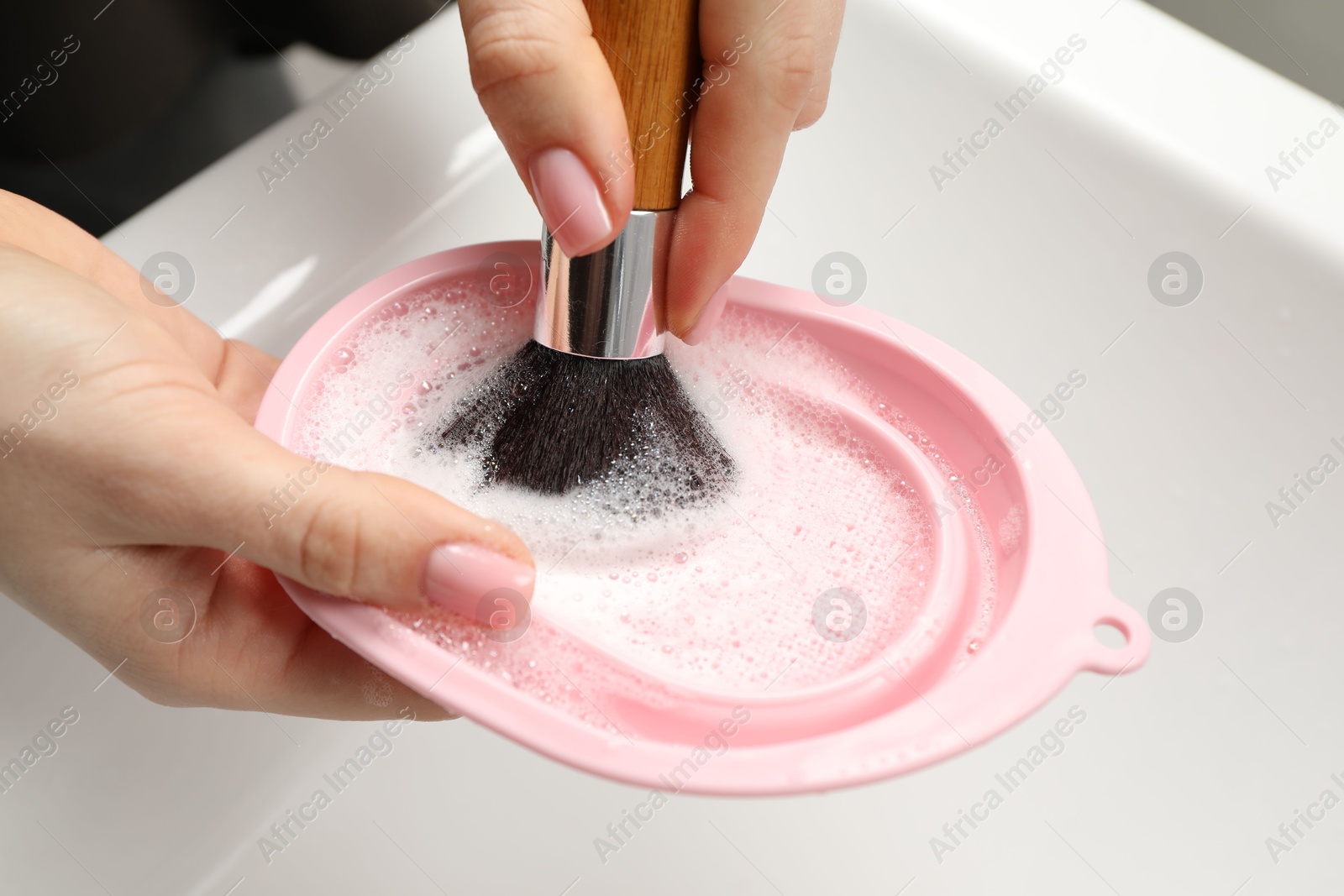 Woman washing makeup brush with soap and cleansing pad over sink, closeup Photo of Woman washing makeup brush with soap and cleansing pad over sink, closeup