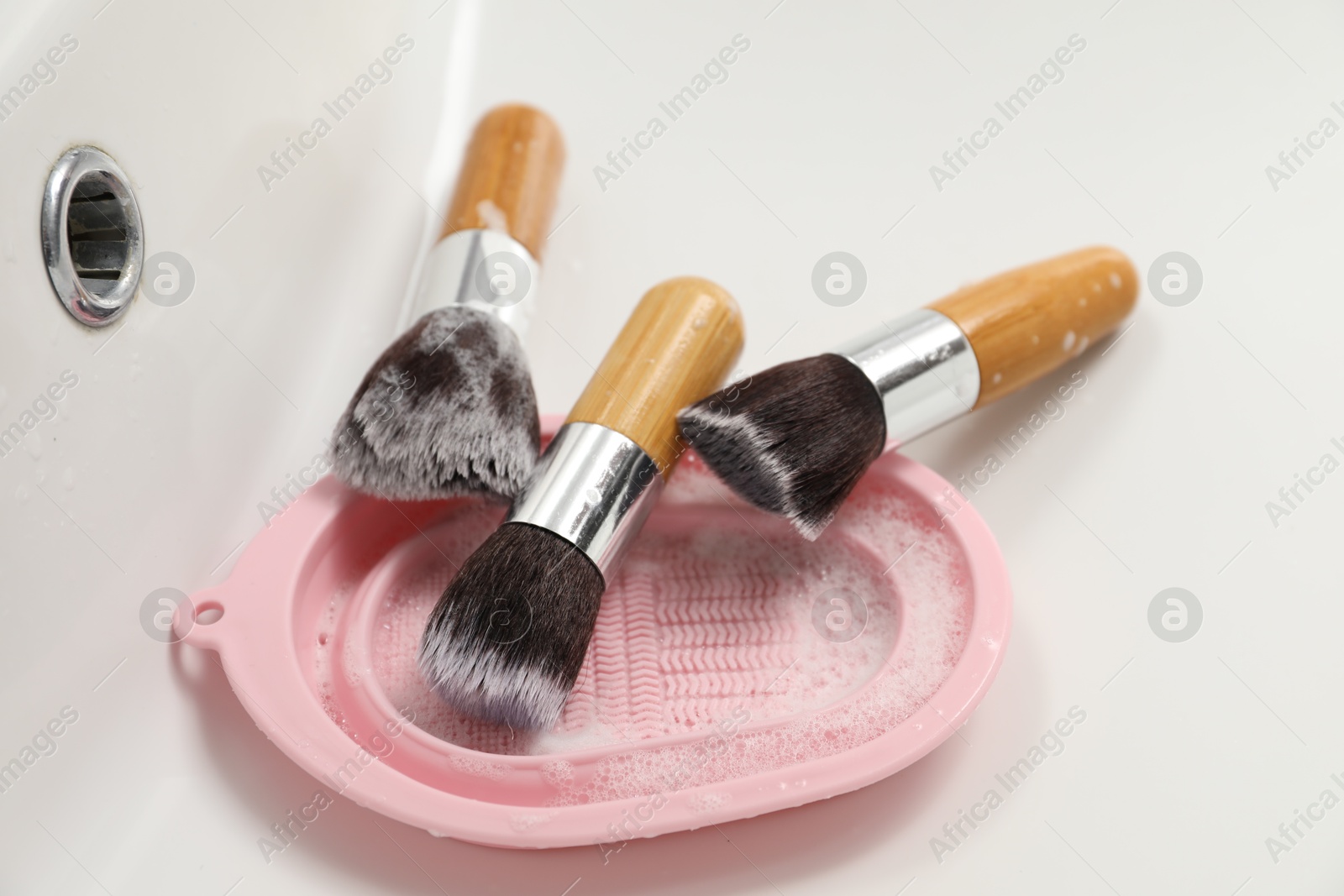 Photo of Makeup brushes with soap and cleansing pad in sink, closeup