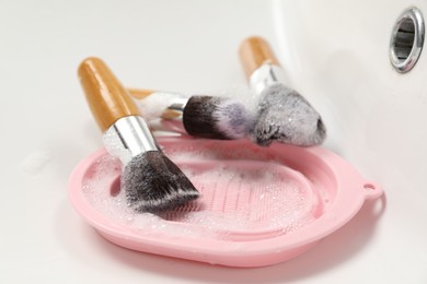 Photo of Makeup brushes with soap and cleansing pad in sink, closeup