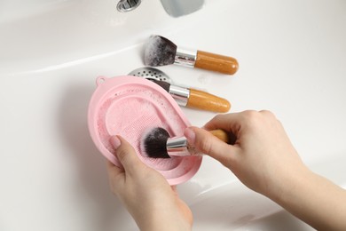 Photo of Woman washing makeup brush with soap and cleansing pad in sink, above view