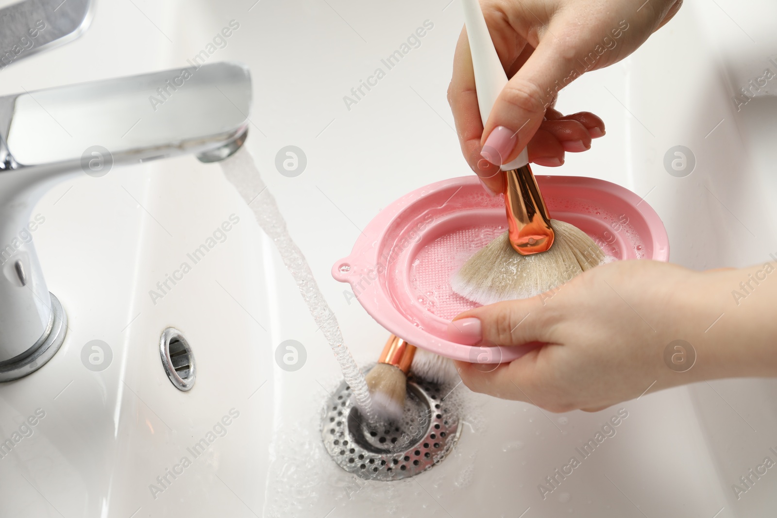 Photo of Woman washing makeup brush with soap and cleansing pad in sink, closeup