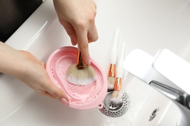 Photo of Woman washing makeup brush with soap and cleansing pad in sink, above view