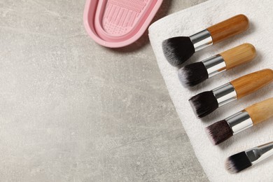 Photo of Clean makeup brushes with towel and cleansing pad on grey table, flat lay. Space for text