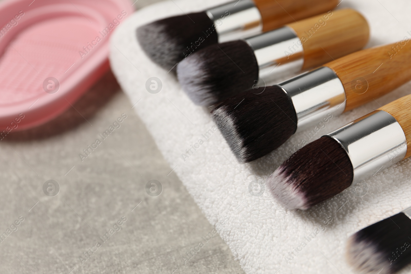 Photo of Clean makeup brushes with towel and cleansing pad on grey table, closeup. Space for text