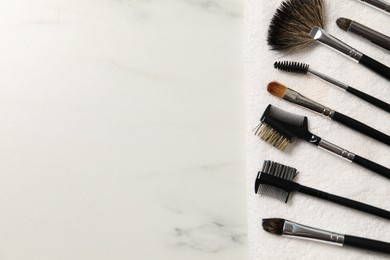 Photo of Clean makeup brushes with towel on white marble table, top view. Space for text