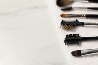 Photo of Clean makeup brushes with towel on white marble table, closeup. Space for text