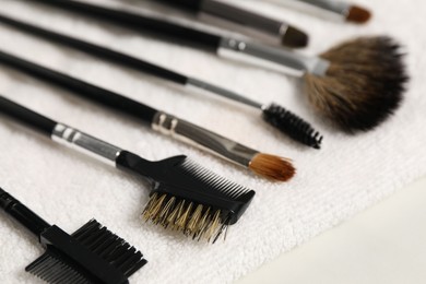 Photo of Clean makeup brushes with towel on white table, closeup