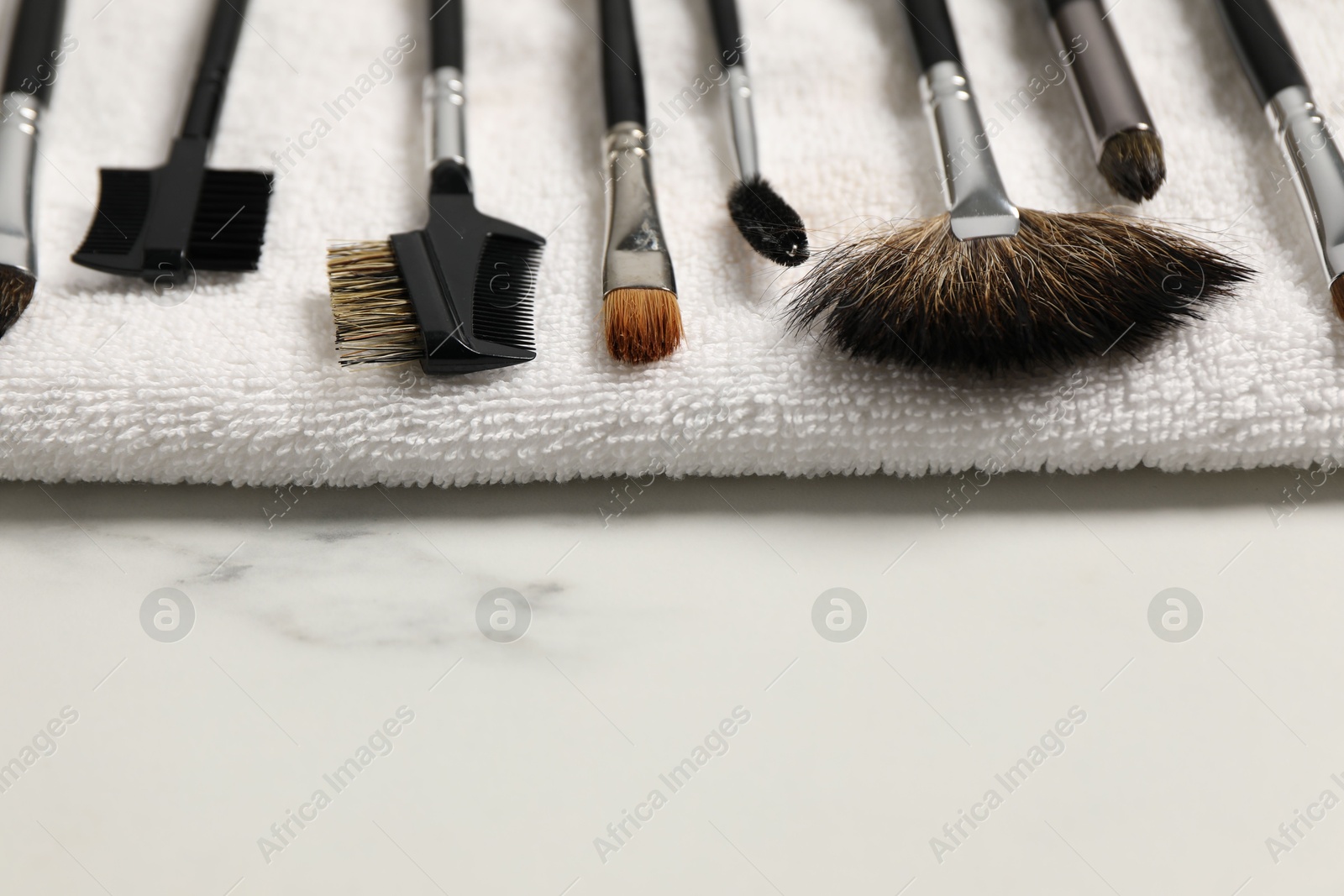 Photo of Clean makeup brushes with towel on white marble table, closeup