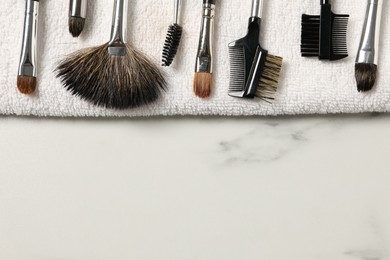 Photo of Clean makeup brushes with towel on white marble table, top view. Space for text