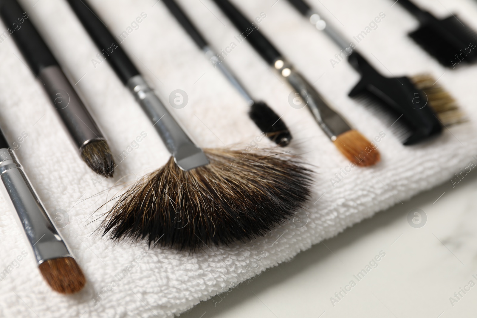 Photo of Clean makeup brushes with towel on white table, closeup