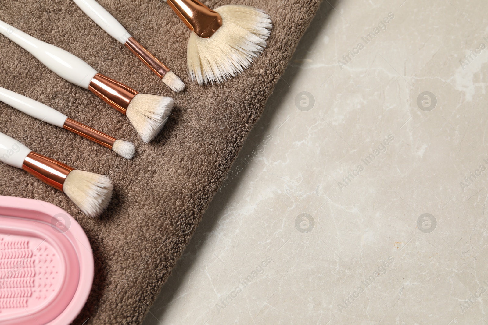 Photo of Clean makeup brushes with towel and cleansing pad on grey marble table, top view. Space for text