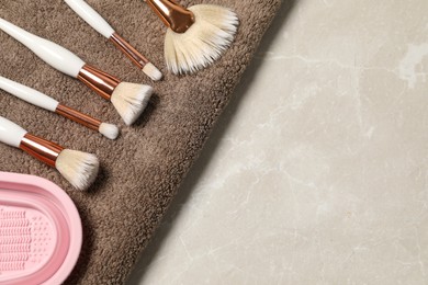 Photo of Clean makeup brushes with towel and cleansing pad on grey marble table, top view. Space for text