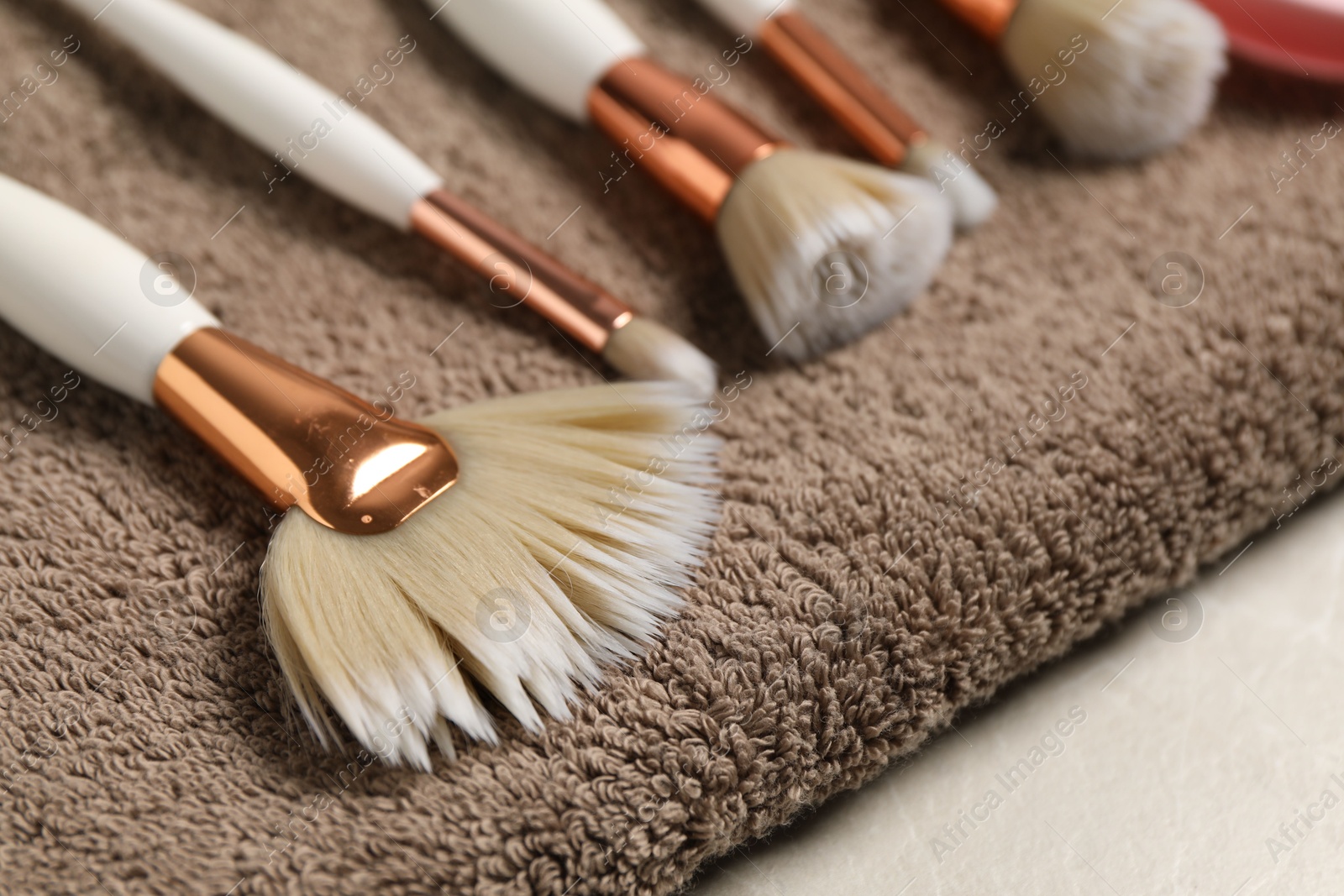 Photo of Clean makeup brushes with towel on grey table, closeup