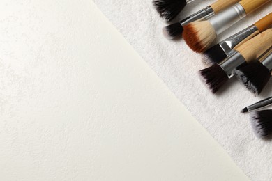 Photo of Clean makeup brushes with towel on white table, top view. Space for text